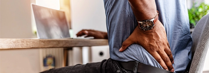 Chiropractic Bellevue WA Back Pain A person sitting at a computer desk, holding their lower back.