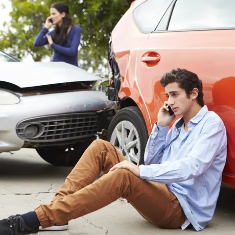 Two people on the phone after a car accident.