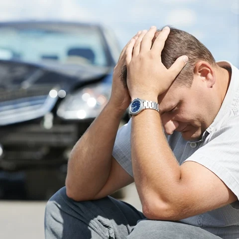 Auto Injury Bellevue WA Man Sitting A man sitting in front of a car after a car accident.